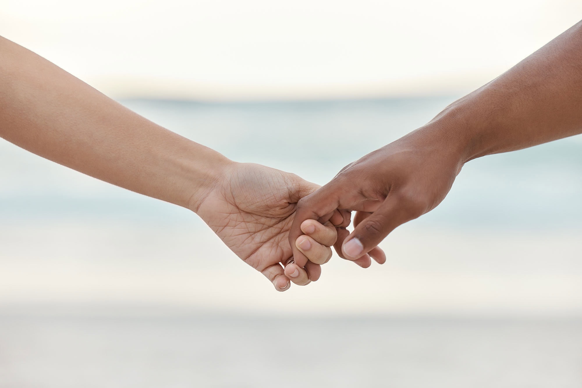 Touch, love and support with interracial couple holding hands in